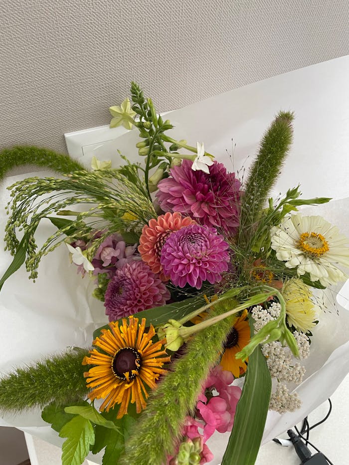 A vibrant floral bouquet featuring dahlias, daisies, and various greenery on a white surface.
